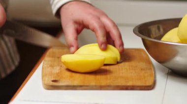 Erkek aşçı sebze yemeği pişirmek için çiğ patates keser, tahta kesme tahtasına patates keser, ev sahibi mutfağında yemek hazırlar, vejetaryen biri için lezzetli bir yemektir.