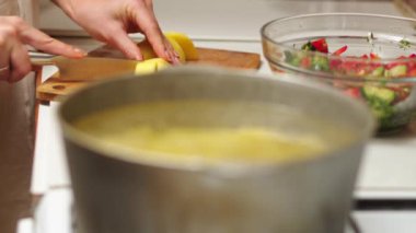 Close up view of woman in white shirt peeling a potato. Peel falling onto cutting board. Lady preparing potatoes to be cut and added to stock pot for dinner.