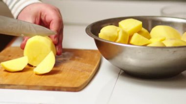 Male cook cuts raw potatoes for cooking vegetable food, cuts potatoes on a wooden cutting board, the hostess prepares food in her kitchen, a delicious dish for a vegetarian