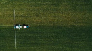 Spraying a green wheat field by tractor. The farming tractor spraying on field with sprayer, herbicides and pesticides. Industrial machine fertilizing a field. Chemicals used by agricultural tractor.