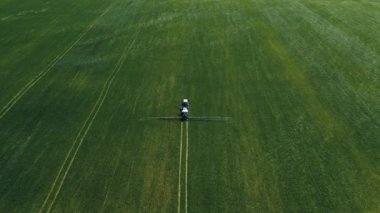 Spraying a green wheat field by tractor. The farming tractor spraying on field with sprayer, herbicides and pesticides. Industrial machine fertilizing a field. Chemicals used by agricultural tractor.