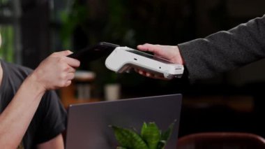 A young man uses NFC smart phone cashless wallet technology to pay for an order at a bank terminal in a beautiful restaurant. Contactless payment.