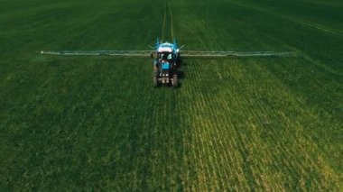 Spraying a green wheat field by tractor. The farming tractor spraying on field with sprayer, herbicides and pesticides. Industrial machine fertilizing a field. Chemicals used by agricultural tractor.