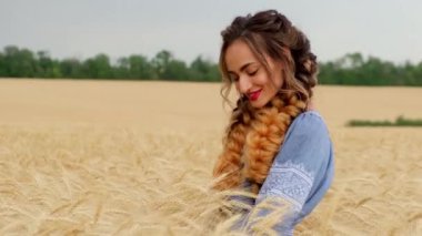 Ukraynalı bir kadın şafak vakti buğday tarlasında yürüyor, elleriyle buğday başaklarına dokunuyor. Tarımda ekinler, yeşil filizler. Özgürlük kavramı. Buğdayın ılık renkleri.