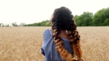Ukraynalı bir kadın şafak vakti buğday tarlasında yürüyor, elleriyle buğday başaklarına dokunuyor. Tarımda ekinler, yeşil filizler. Özgürlük kavramı. Buğdayın ılık renkleri.