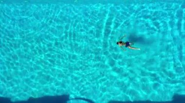 Yüzme havuzunda dalgalı bir su yüzeyinde yüzen genç bir adamın yukarıdan aşağı hava görüntüsü. Adam havuzda rahatlıyor. Yüksek açı görünümü