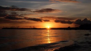 Denizin üzerindeki güneş. Plaj palmiyeleri adasında inanılmaz kırmızı gün doğumu. Turuncu renkler gündoğumu ve dalgalar. Doğanın güneş doğuşu palmiyelerin plaj arka planı. Sarı gökyüzü, plaj adasında güzel palmiye ağaçları. Güneş ışığı