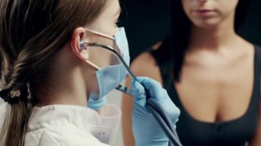 Üniformalı genç bir kadın doktor, fonendoskoplu genç bir kadını muayene ediyor. Derin nefes alırken ciğerlerini dinliyor. Evdeki tıbbi konsültasyon sırasında kanepede oturmak. Yakın plan.