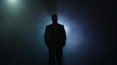 Sahnede takım elbiseli bir adamın silueti. Mistik atmosfer, duman, spot ışıkları. Karanlıktaki kişi.