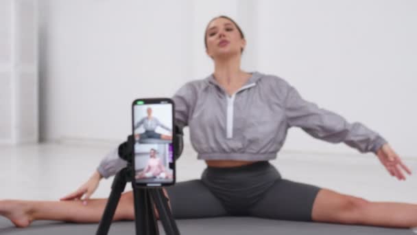 年轻健康的欧洲女性记录视频博客坐在瑜伽工作室的垫子上 瑜伽教练与订户交谈并解释练习 体育博客的概念 — 图库视频影像