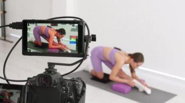 Cinematic shot of young sporty brazilian woman with athletic body wearing bra and leggings is practicing workout exercises for legs and buttocks on fitness mat with online tutorial on laptop at home.