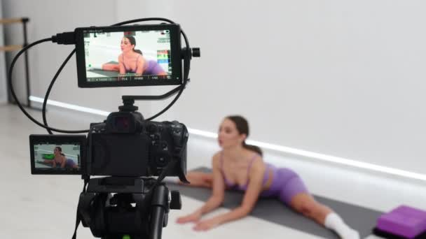 ブラジャーとレギンスを身に着けている運動体を持つ若いスポーティなブラジル人女性の映画撮影は自宅でラップトップ上のオンラインチュートリアルでフィットネスマットで足やお尻のためのワークアウトの演習を練習しています — ストック動画