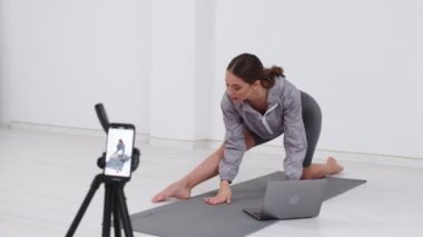 Genç Kız Spor Videosunu Çekiyor. Genç kız blog yazarken çevrimiçi eğitime uzaktan eğitim veriyor. Parlak Odada Mat Üzerinde Esneme Egzersizleri Yaparken Kız Video Blog Çekiyor.