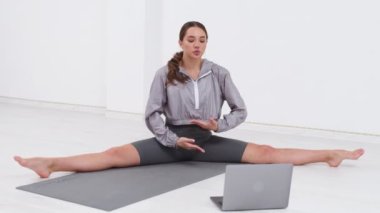 Young athletic woman trainer exercising, stretching and doing yoga. Online fitness training through laptop computer.