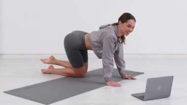 Genç atletik kadın antrenör egzersiz yapıyor, esniyor ve yoga yapıyor. Dizüstü bilgisayarla çevrimiçi fitness eğitimi.