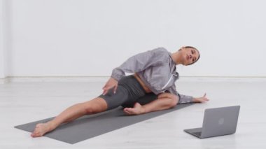 Young athletic woman trainer exercising, stretching and doing yoga. Online fitness training through laptop computer.