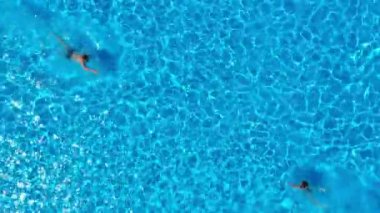 Drone view of a couple relaxing, swimming in the pool. Two people enjoy summer holidays, weekends. Aerial view of multiracial couple relaxing in clear blue water of hotel swimming pool