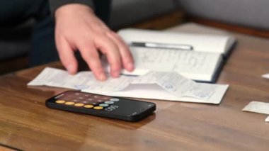 a young man in the living room sofa accounting for financial expenses and settling debts using a calculator for calculating income from financial and tax documents in the modern economy