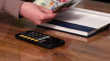 Tanınmayan bir kadının, gri ahşap bir masada 100 dolarlık banknotları saymasının yan görüntüsü. Para, yatırımlar, para değişimi, rüşvet, maaş, ödeme, finans, iş, bankacılık, tasarruflar.