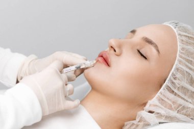 close-up, female lips. Surgeon, in medical gloves, carefully and slowly injects hyaluronic acid into woman's lips with a syringe. lip augmentation procedure. beauty injections. Plastic surgery.