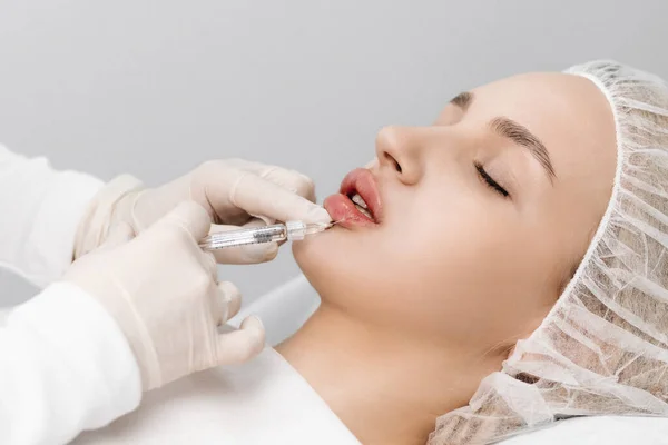 close-up, female lips. Surgeon, in medical gloves, carefully and slowly injects hyaluronic acid into woman\'s lips with a syringe. lip augmentation procedure. beauty injections. Plastic surgery.