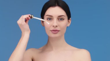 close-up of an attractive European young woman applies a face care serum to her cheek from a pipette. Facial serum advertisement