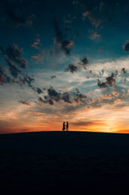 Mutlu genç bir çiftin siluetleri. Kum çölünde, turuncu günbatımının arka planında.