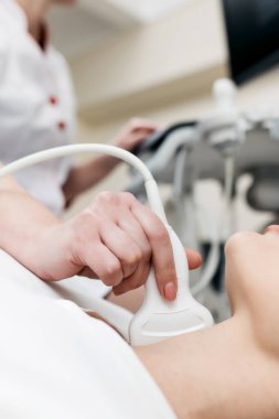 Doktor, hastanın tiroid bezini ultrason tarayıcısı yardımıyla teşhis etti. Kadın kanepede yatıyor. Bir kadın klinikte hastanın boynunda ultrasonik sonda tutuyor..