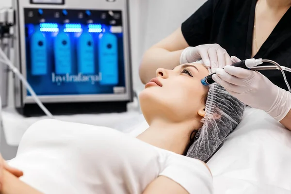 Kozmetoloji kliniğindeki güzel kadın hastalara hidro soyma işlemi yapan tıbbi eldivenler giyen profesyonel bir dermatolog. Yüz tedavisini kapat.
