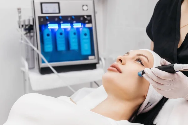Cosmetologist doing hydrafacial treatment on woman face in beauty clinic
