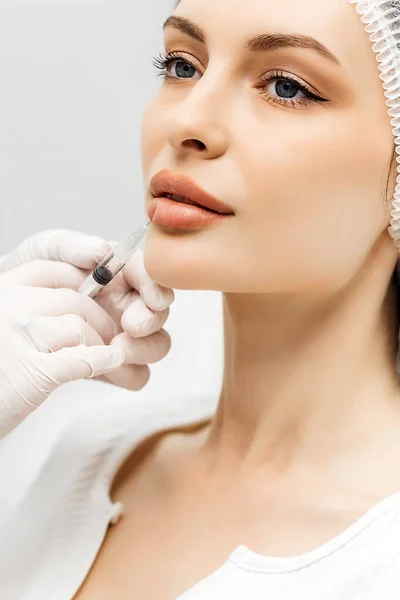 Çekici genç bir kadın canlandırıcı yüz enjeksiyonu yaptırıyor. O, klinikte sakince oturuyor. Uzman güzellik uzmanı hyaluronik asitle kadın kırışıklıklarını dolduruyor..