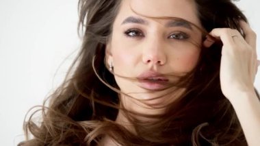 Genç kadın beyaz arka planda gözlerini aç. Stüdyoda kameraya bakan gülümseyen kıza yaklaş. Kıvırcık saçlı manken yüzü gülümsüyor. Neşeli kızın portresi, açık gözler. Kadın doğası güzelliği