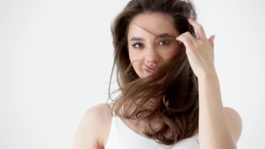 Şatafatlı, kendine güvenen, uzun dalgalı saçlı, göz kalemi makyajlı, beyaz arka planda poz veren güzel esmer kadın. Yakın çekim stüdyo portresi. Güzellik konsepti. Saç bakım konsepti, reklamcılık.