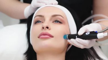 Doktor kozmetolojistin kozmetoloji ofisinde yaşlanmayı önleme prosedürü uygulaması. Tek kullanımlık şapkalı tatmin olmuş kadın kanepede uzanıyor ve dinleniyor. Aygıtla çalışmak.