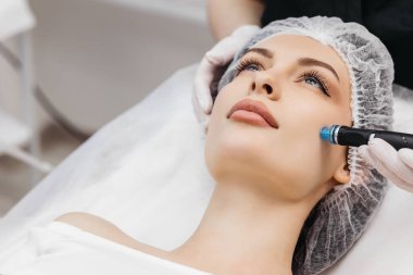 Cleansing procedure. Nice pretty woman lying with her eyes closed while having a cleansing procedure on her face clipart