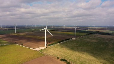 Kuş bakışı bir tarlada bıçakları olan büyük rüzgar türbinleri. Yel değirmenlerinin siluetleri, büyük bir turuncu güneş diski, yaz alevleri. alternatif enerji