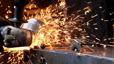 Fabrika işçisi metali kaynaklıyor. Adam kaynak yapıyor. Kaynak makinesi kullanarak argon veya elektrot ile kaynak yapmak. Metal yapılar üreten bir endüstriyel girişim. Kıvılcımlar ve parıltılar uçuşuyor.