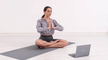 Young athletic woman trainer exercising, stretching and doing yoga. Online fitness training through laptop computer.