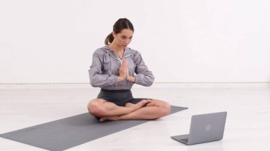 Young athletic woman trainer exercising, stretching and doing yoga. Online fitness training through laptop computer.