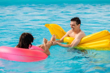 Yüzme havuzunda yüzen, konuşan ve rahatlatan mutlu genç çift.