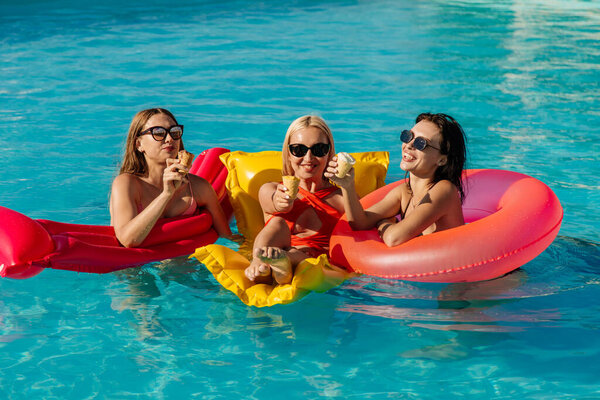 A group of beautiful, young women are eating strawberry popsicles and having fun in the pool.