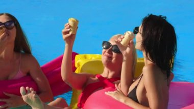 Bir grup güzel genç kadın, güneşli bir yaz gününde dondurma yiyor ve havuzda eğleniyorlar. Rahatlama, dinlenme ve keyif kavramı