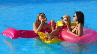 Bir grup güzel genç kadın, güneşli bir yaz gününde dondurma yiyor ve havuzda eğleniyorlar. Rahatlama, dinlenme ve keyif kavramı