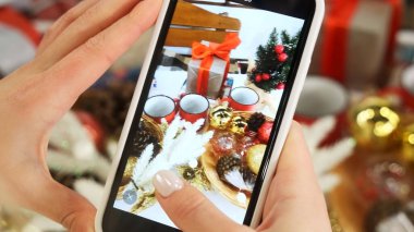 Mutlu Noeller. Akıllı telefonlu bir kadın eli Noel ağacını süslemek için yılbaşı hediyelerinin fotoğraflarını çeker. Noel ve yeni yıl kutlaması. Yüksek kalite fotoğraf
