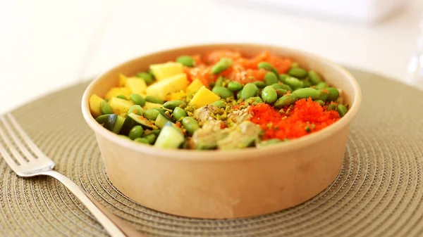 Poke bowl with salmon, rice, avocado, edamame beans, cucumber and radish in gray bowl. Hawaiian ahi poke bowl, gray background.