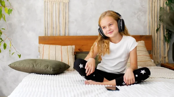 Happy little girl dances and listens favourite track in headphones at home
