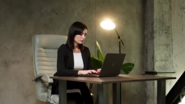 Başarılı kadın grafikçi tasarımcı ofiste çalışırken dizüstü bilgisayarda yaratıcı fikirler hakkında özel ders izliyor. Amerikalı kadın sandalyede otururken dizüstü bilgisayar kullanıyor.