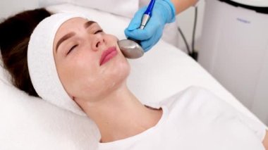 Kozmetik uzmanı modern güzellik kliniğinde RF kaldırma prosedürü uyguluyor. Kadın müvekkil yüz bakımını canlandırıyor. Teni gençleştirme, yaşlanmayı önleme kavramı.