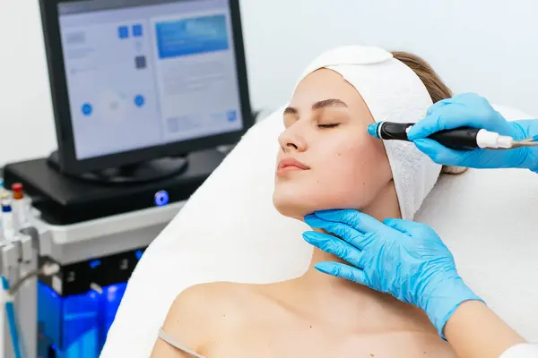 stock image Professional female cosmetologist doing hydra-facial procedure in cosmetology clinic. Doctor using hydra vacuum cleaner. Rejuvenation and cosmetology concept