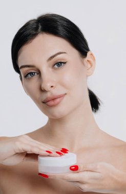 Mükemmel sağlıklı cilde sahip beyaz bir kadının güzel yüzü bir ürün teklif ediyor. Beyaz arka planda sabun ve krem modelleri olan bir kız. Reklam için jestler.